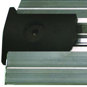 Close-up of a metallic linear rail system with a black carriage block featuring a grooved design. It includes the Quantum End Stop Kit with two end stoppers and a drill bit for precise alignment. The block partially covers the rail, showcasing a recessed center hole.
