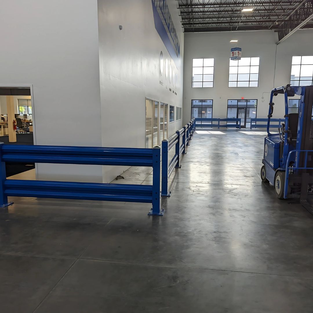 Blue steel warehouse guard rail separating a forklift travel aisle from pallet racking