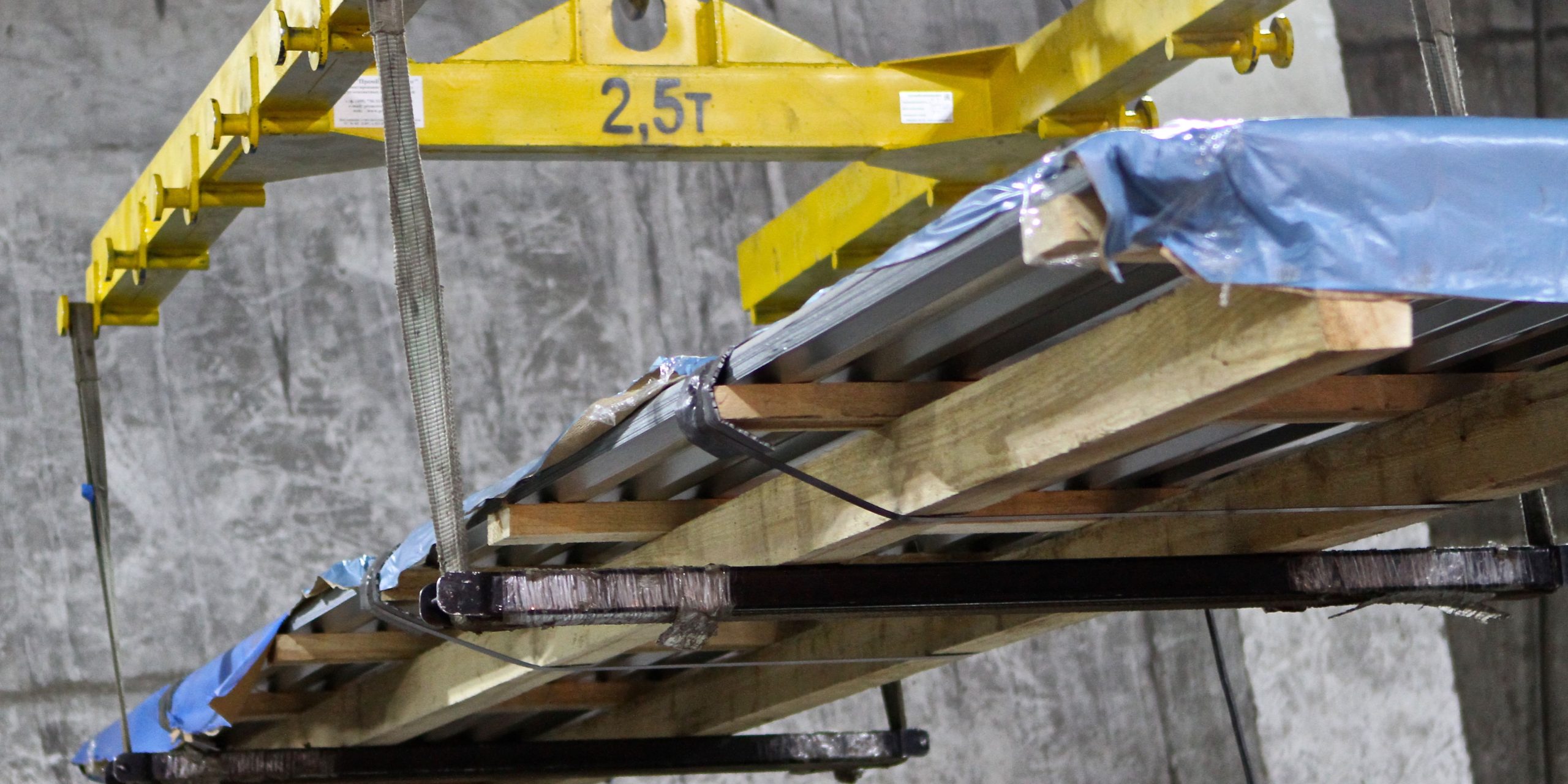 A yellow lifting crane hoisting a load of wood