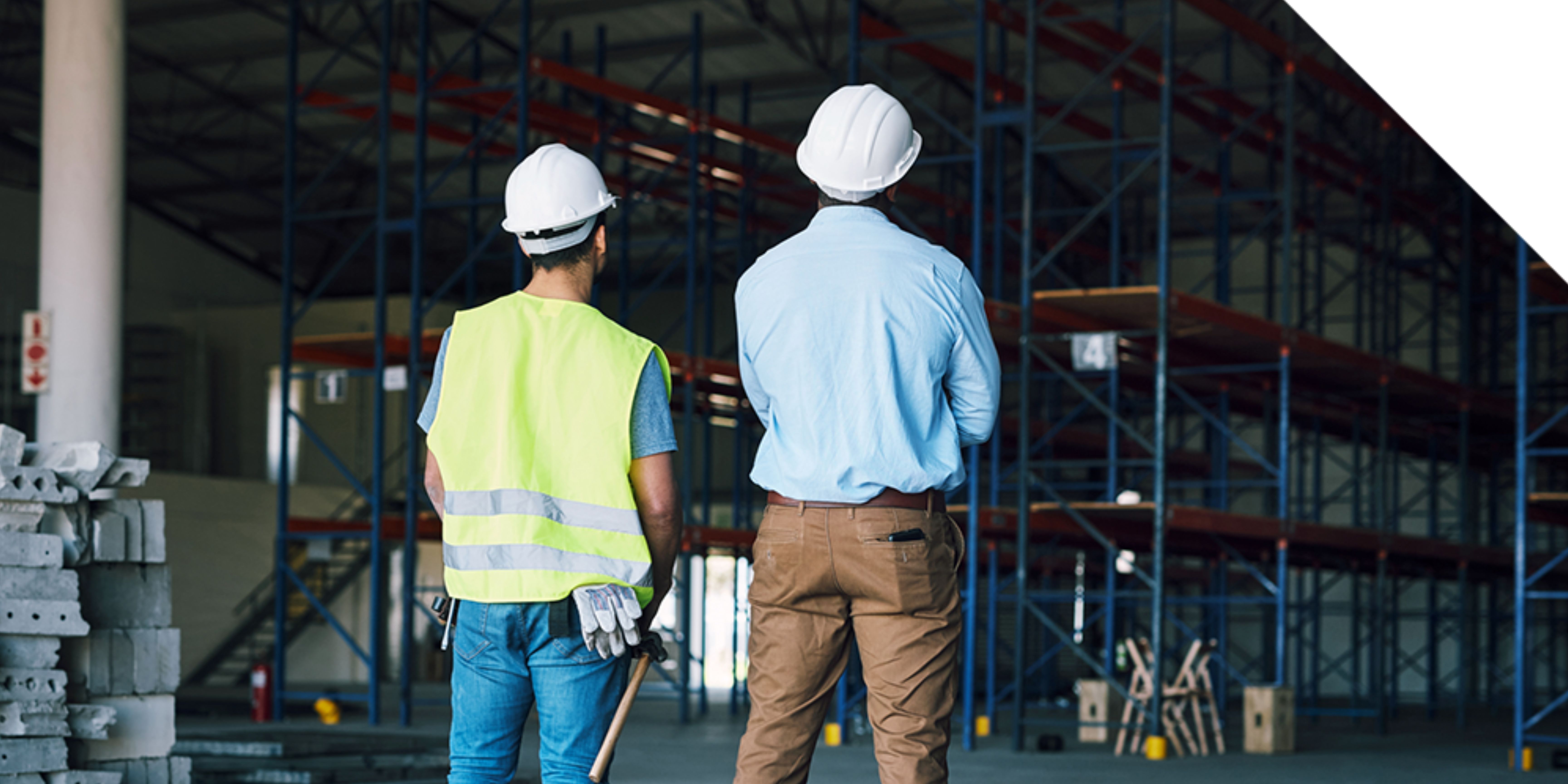 Two specialists in hard hats walking a warehouse aisle to document racking, clear height and column spacing