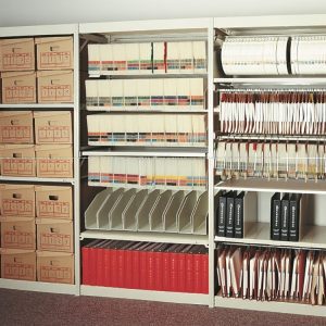 An E-Z-Rect shelving storage solution brims with organized files and folders. The left section features labeled cardboard boxes, the middle displays colorful binders and slots, and the right hosts hanging folders and binders, all set against a light-colored wall.