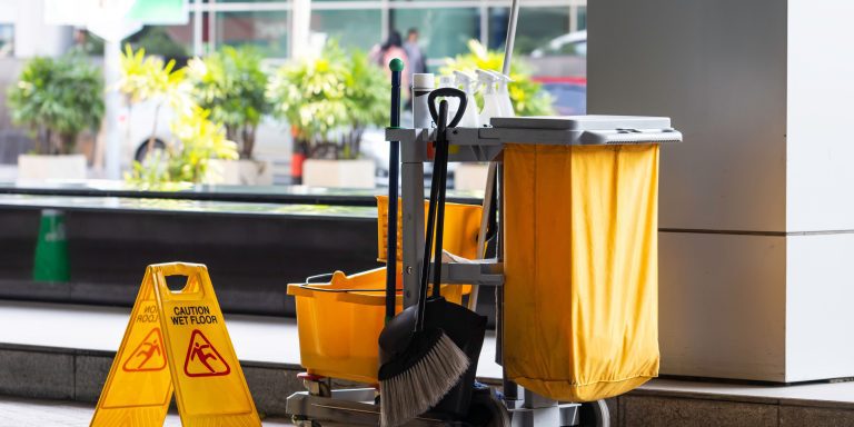 Janitorial cart loaded with cleaning supplies and a mop in a facility corridor