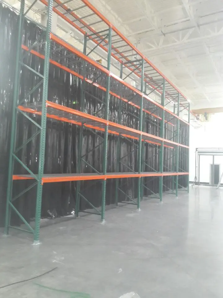 Tall warehouse pallet racking with orange beams and wire decking, demonstrating best practices for seismic-compliant pallet racks in large storage facilities.