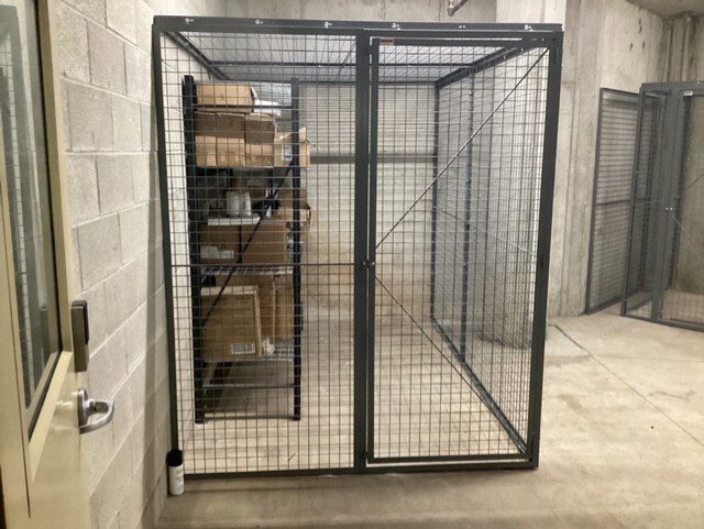 Metal storage cage with boxes on shelves inside, set in a concrete room.