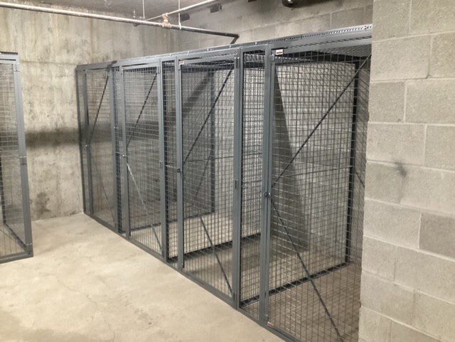 Metal storage cages in a concrete room, some empty and others holding shelves with boxes.