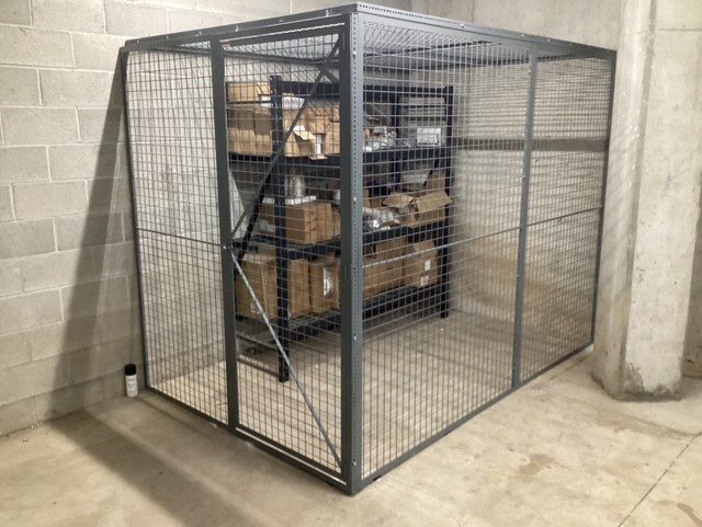 storage cage with shelves holding boxes inside, located in a concrete room.