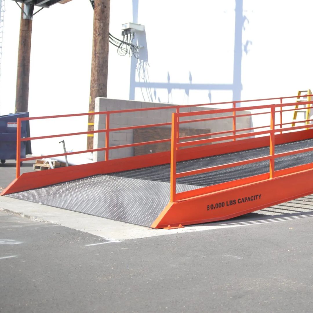 Orange steel dock ramp with safety railings positioned at a loading dock for material handling equipment