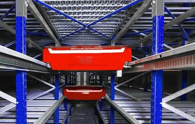 Red Quadron shuttle moving between storage racks in an automated warehouse system for cartons and totes.