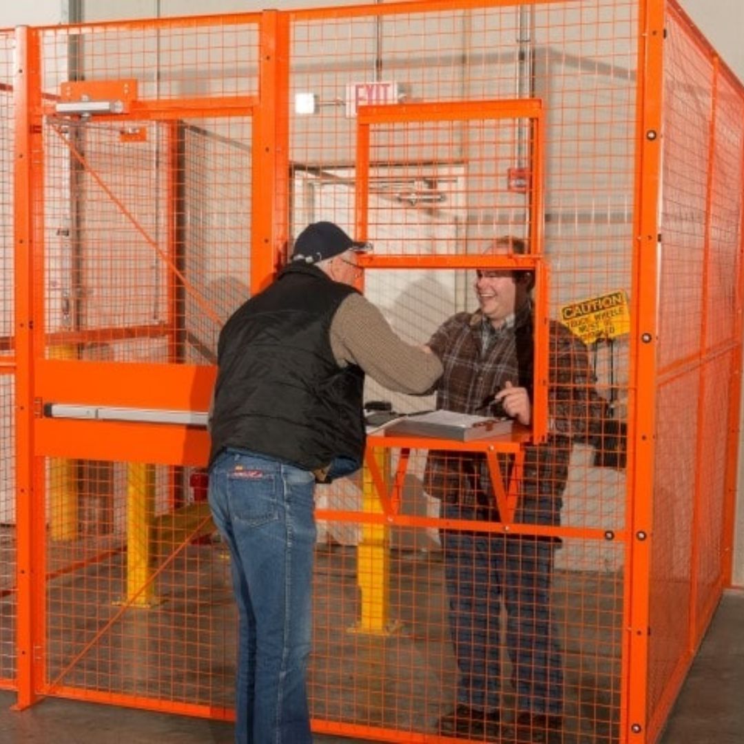 Two workers passing materials through a service window in an orange wire mesh partition