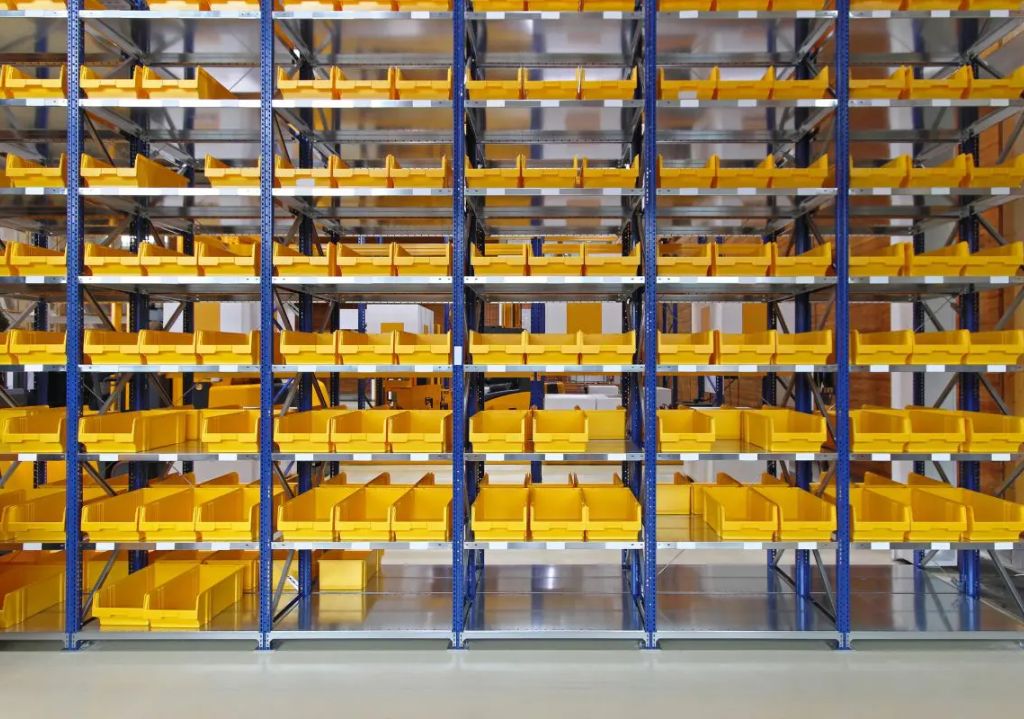 Rows of metal Equipto and Borroughs Shelving filled with empty yellow Small Parts Organizer Bins are arranged in a warehouse, creating a striking pattern of repeating lines and vibrant colors.