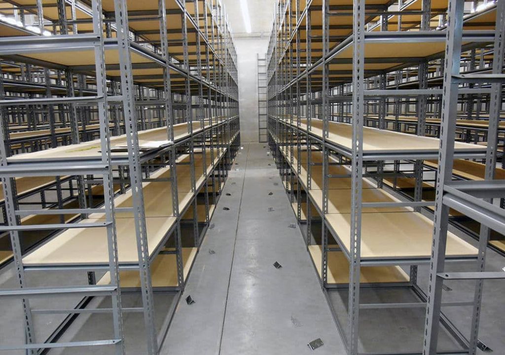Rows of empty Heavy Duty Parts Shelving line both sides of a wide, clean aisle in a warehouse or storage facility with a concrete floor and bright overhead lighting, ideal for Industrial Parts Storage.