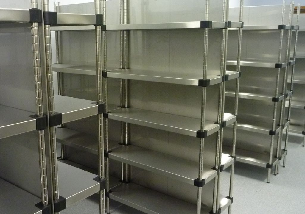 Several empty metal shelving units, ideal for Industrial Parts Storage or outfitted with Small Parts Organizer Bins, are arranged in rows in a clean indoor space with a light-colored floor and walls. Perfect for Equipto and Borroughs Shelving systems.