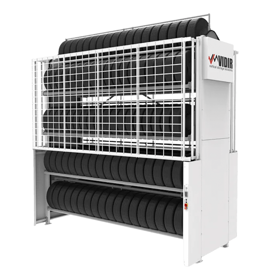A vertical tire carousel storage system by Vidir Vertical Storage Solutions holds multiple rows of black tires, enclosed in a white metal frame with a mesh safety guard and labeled VIDIR on the side.