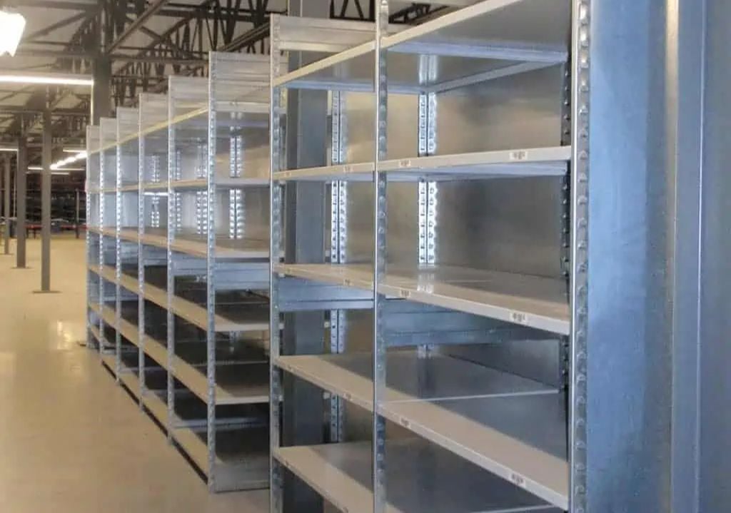 Rows of large, empty metal shelves—ideal for Industrial Parts Storage—stand in a well-lit warehouse, featuring concrete floors and exposed ceiling beams. Equipto and Borroughs Shelving provide durable solutions for organized Part Shelving needs.