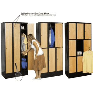 A woman opens a tall Hallowell locker with red oak doors and a black steel frame, revealing shelves with clothes and sports gear. Two similar lockers stand beside her, one open, displaying folded towels and hanging shirts. A tennis racket lies on the floor.