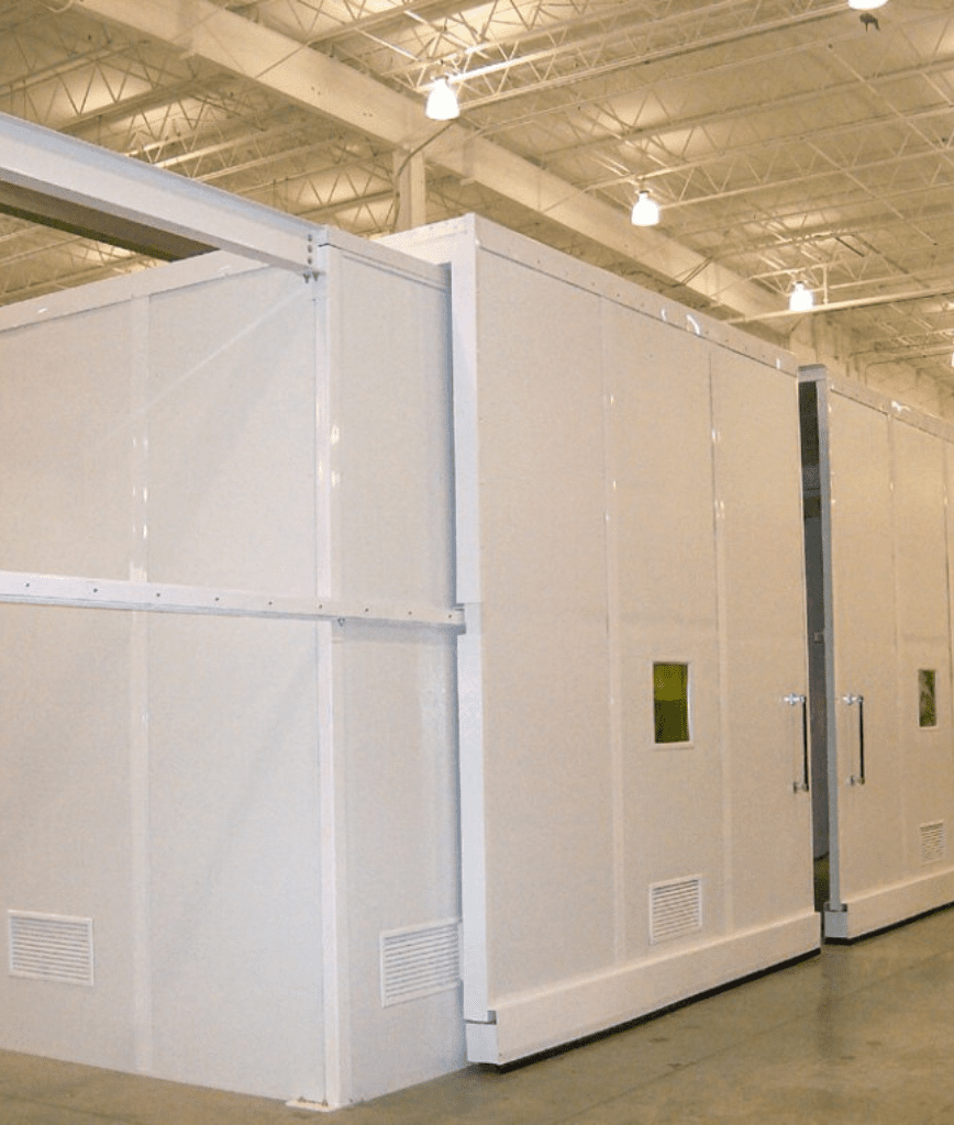 Large white modular cleanroom structure with vents and small windows, located inside a spacious industrial facility with high ceilings and exposed lighting.