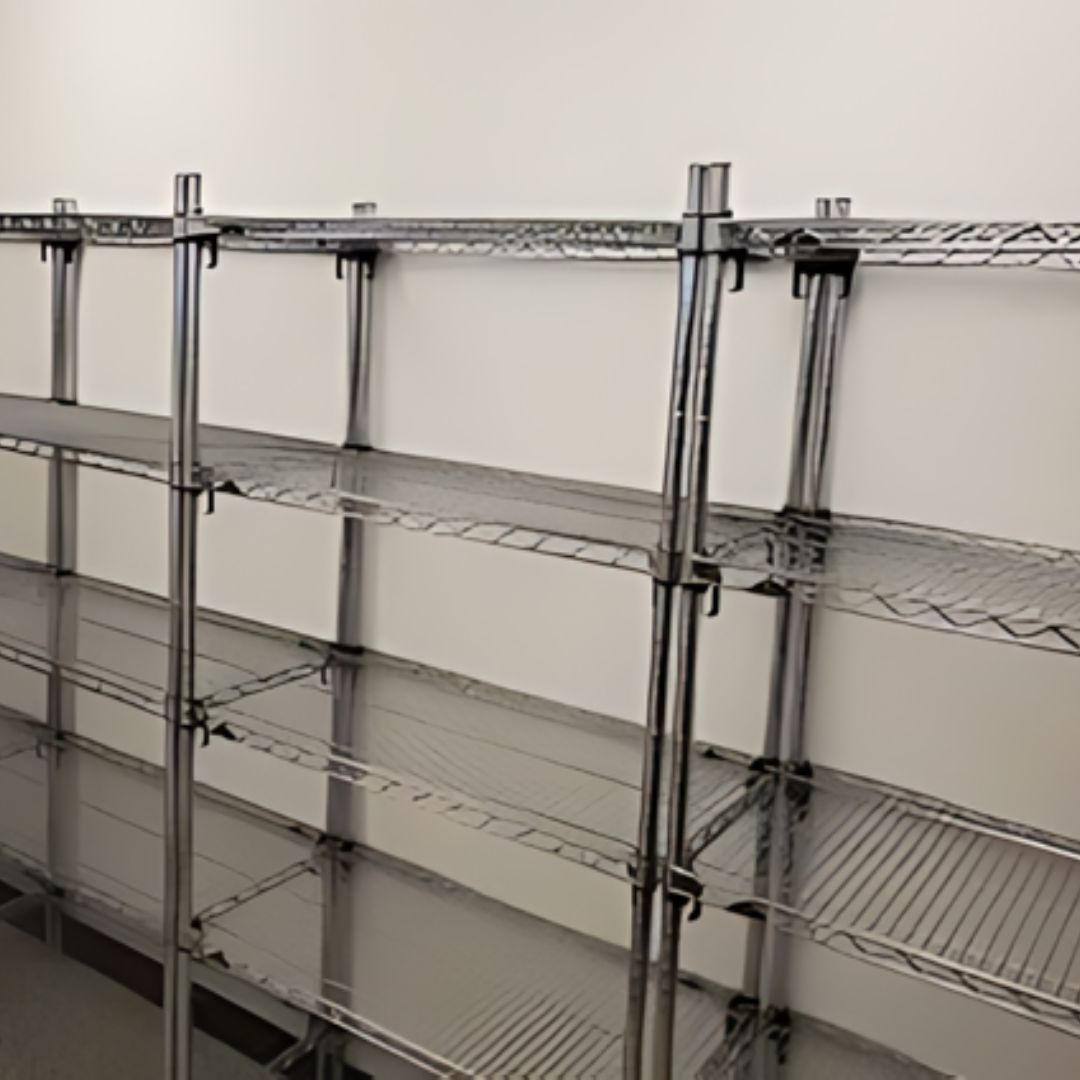 Empty adjustable wire shelving units are arranged against a plain white wall in a clean, well-lit room. The shelves are bare, with no items or decorations placed on them.