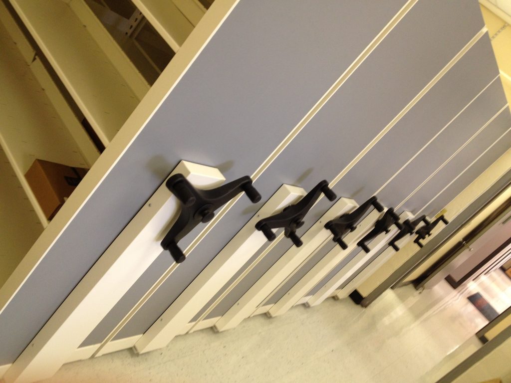 Close-up of mobile shelving carriages with three-spoke handles and blue laminate end panels at Palm Beach Resource Recovery