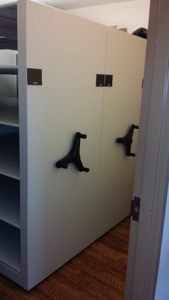 Open aisle between mobile shelving ranges with overhead light fittings visible above