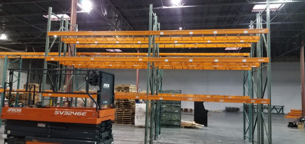Wide view of pallet rack with Aichi scissor lift during installation at Baileys Moving warehouse