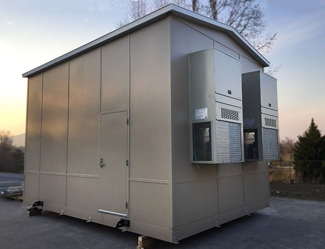 Prefabricated electrical house with wall-mounted air conditioning units on a prepared exterior pad