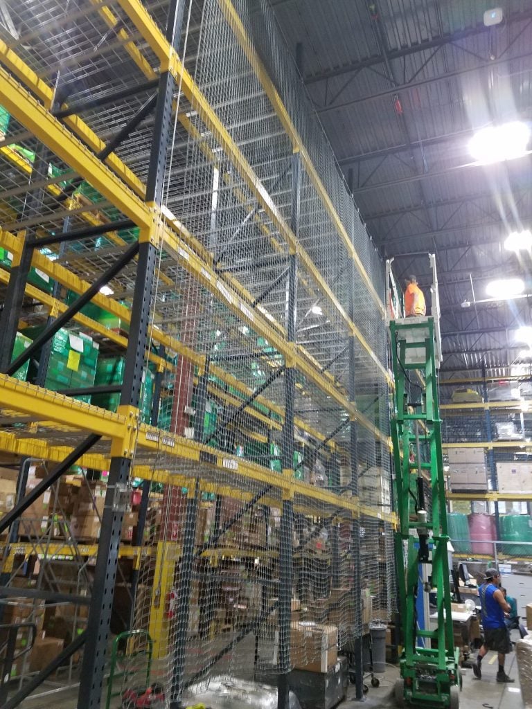 Installer on a lift attaching black safety netting to the back of pallet racking at a Salt Lake City distribution warehouse