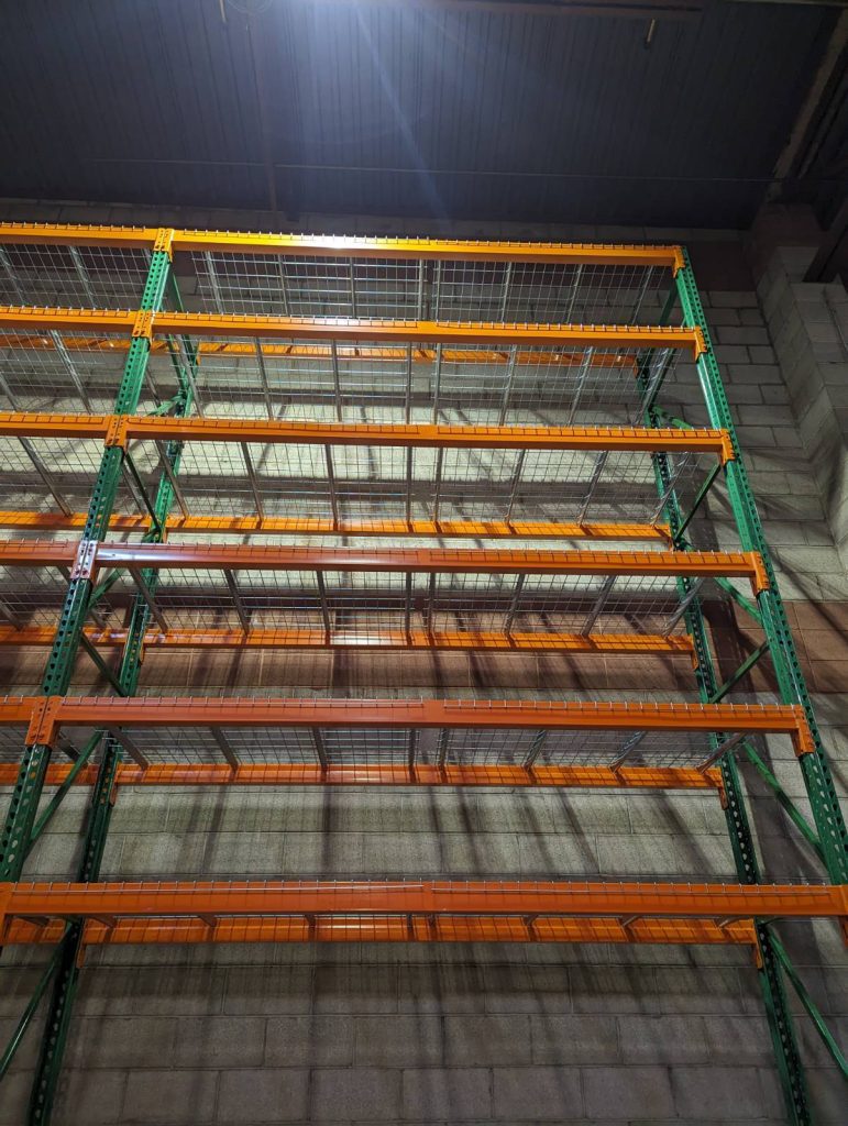 Looking up at new green pallet rack uprights with orange beams and wire decking at Motion Industries