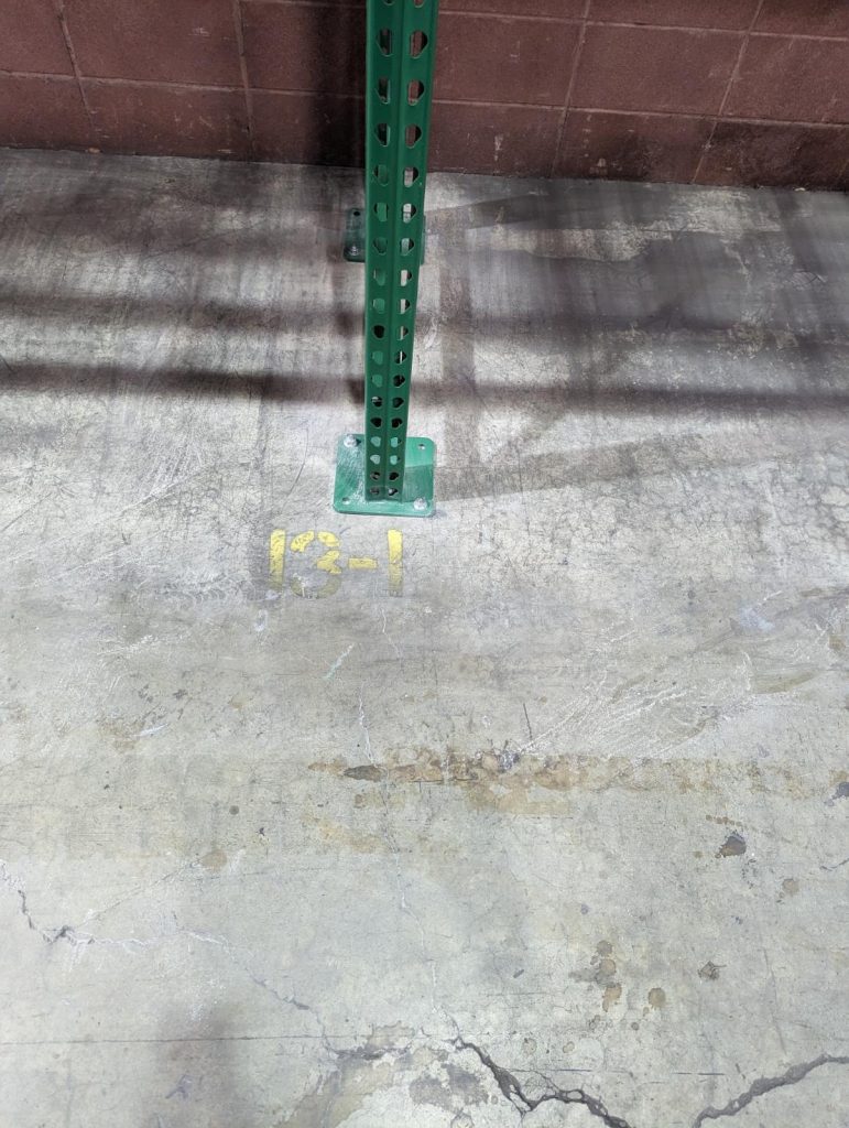 New green pallet rack upright with fresh baseplate anchored to concrete floor at Motion Industries