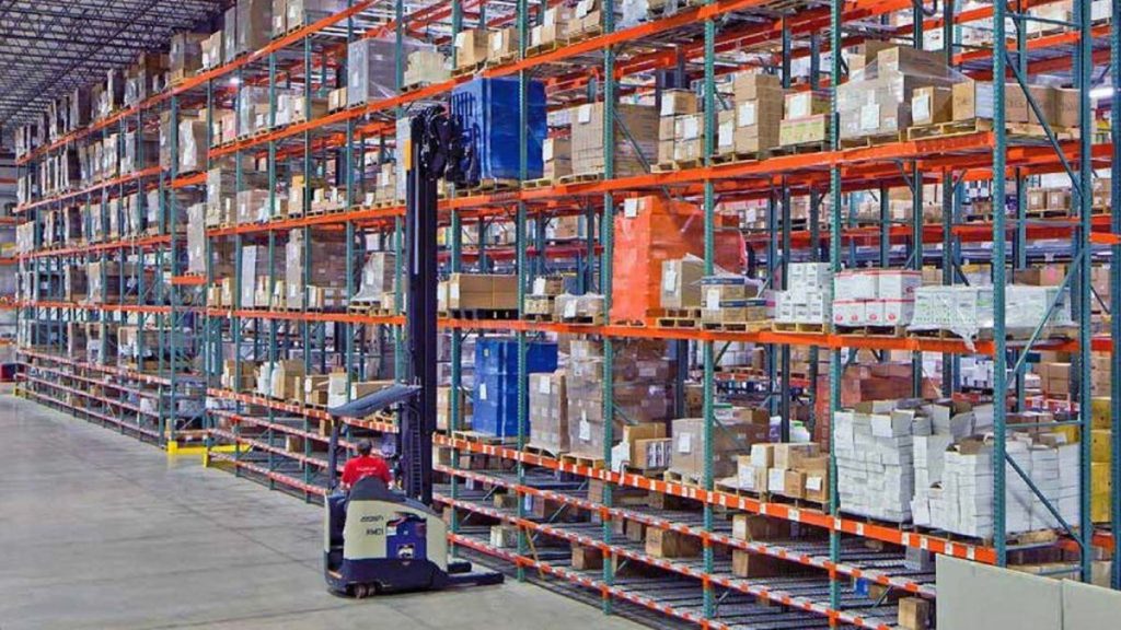 Selective pallet rack rows loaded with palletized goods and a reach truck in the aisle