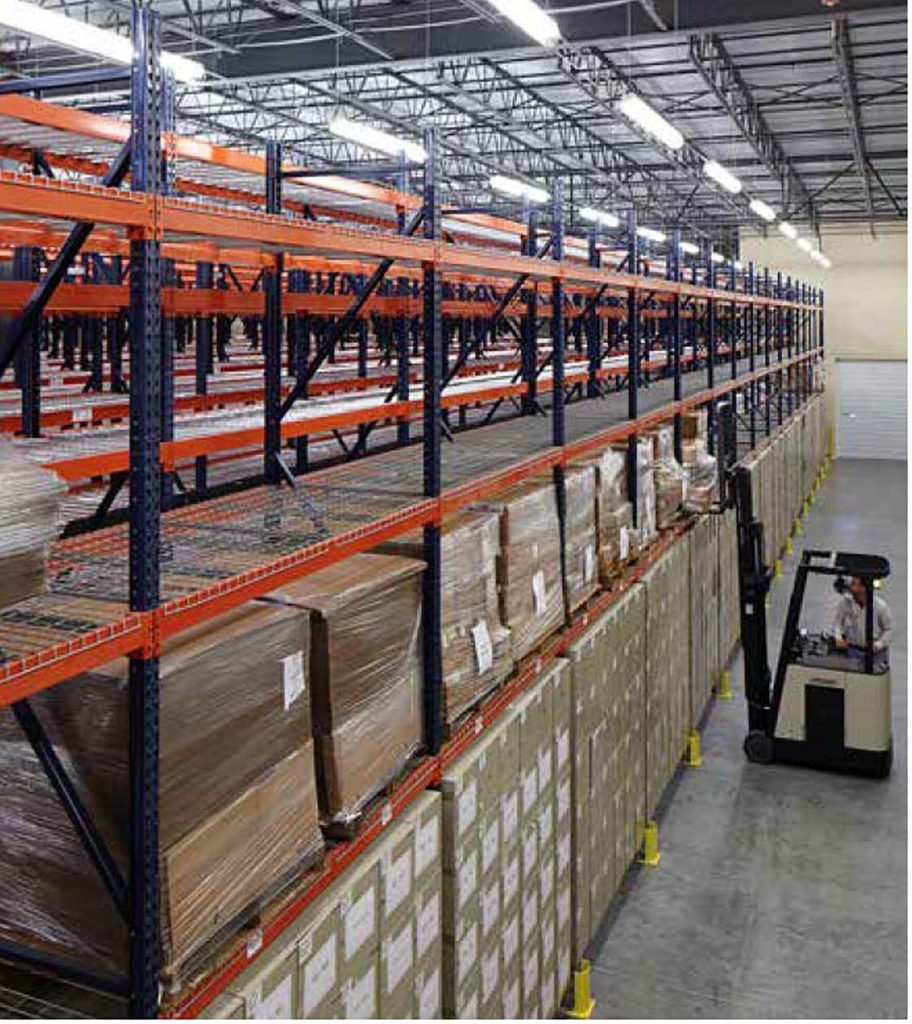 Narrow warehouse aisle between tall pallet rack rows with a reach truck operator working the lane