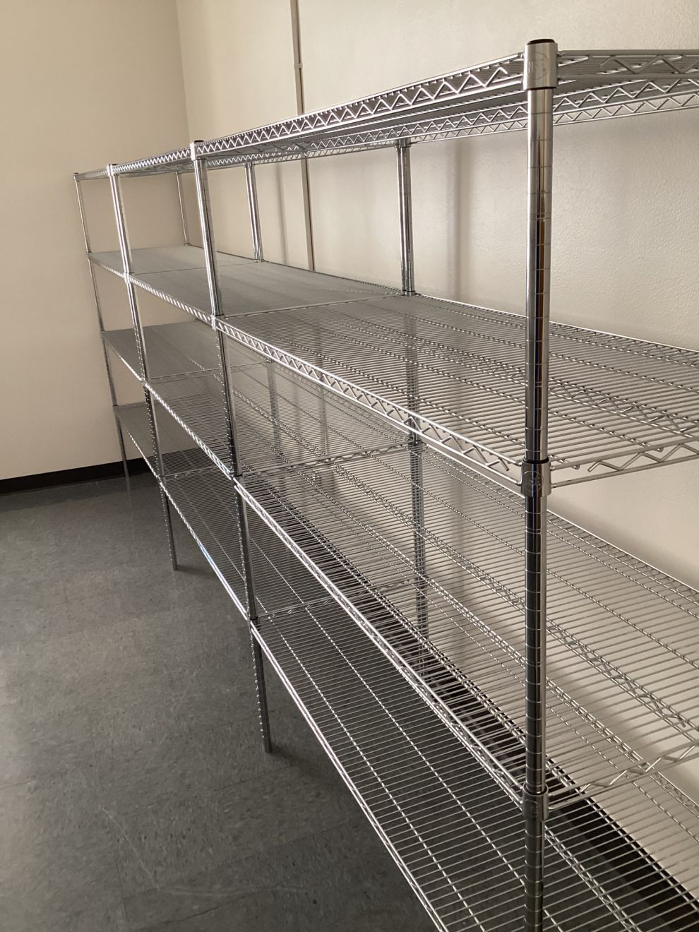 Long continuous run of chrome wire shelving bays sharing posts along a facility wall