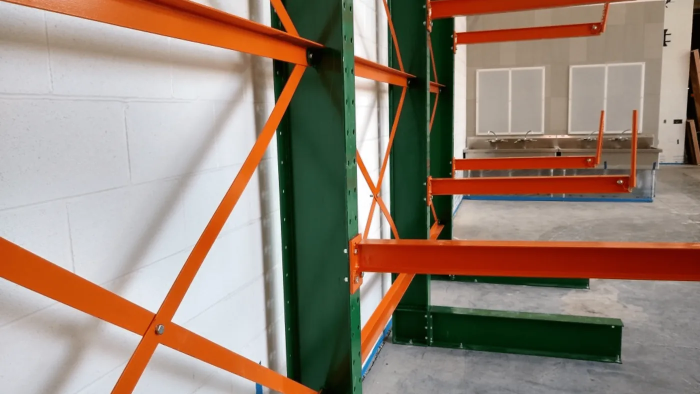 Single-sided cantilever rack with green columns and orange arms installed against a wall at a Utah junior high school