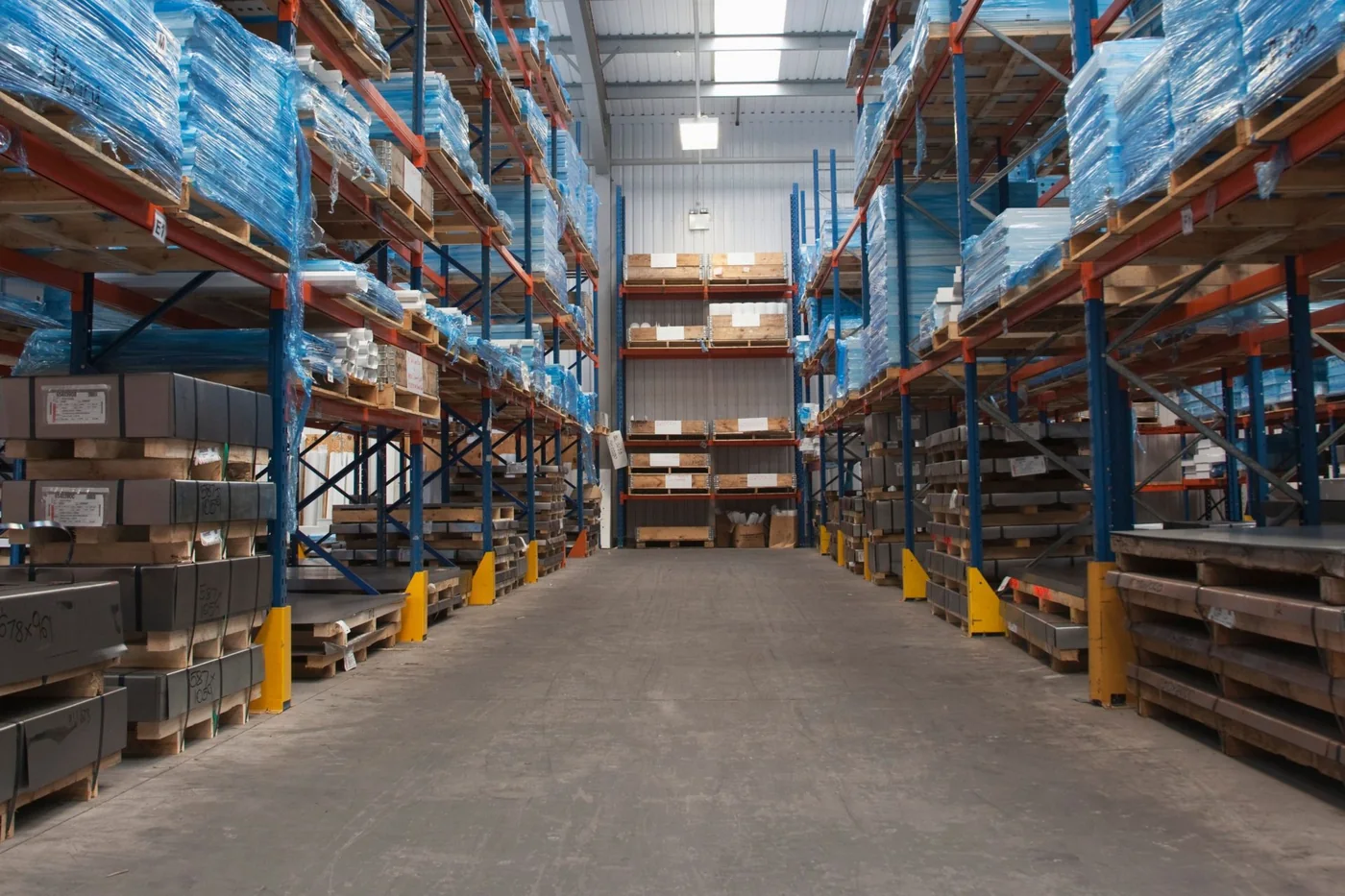 Warehouse pallet rack aisle with yellow and orange column protectors guarding every upright base