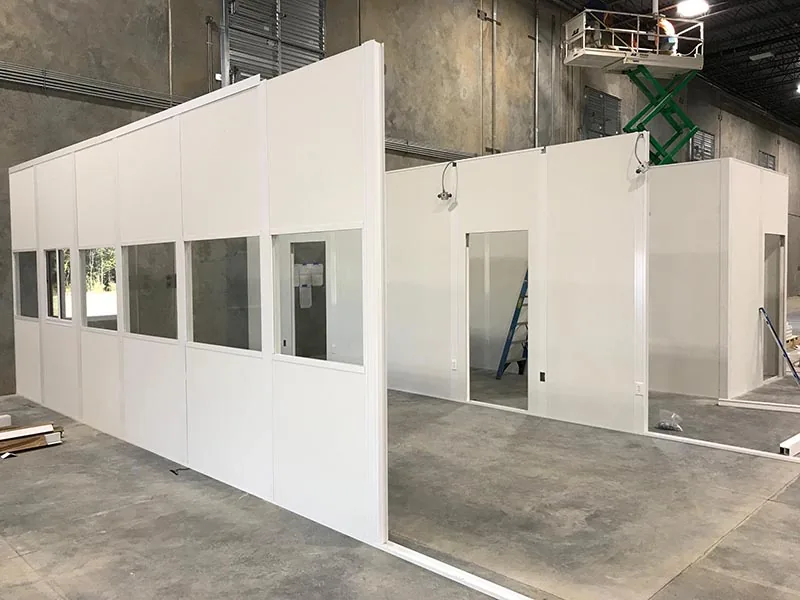 Installation crew erecting white modular office wall panels with vision glazing inside an industrial building