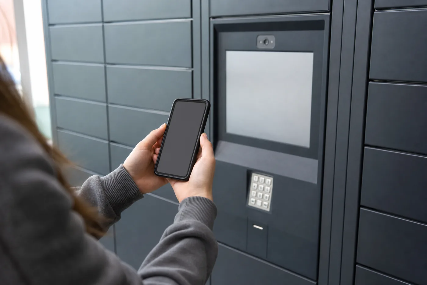 Student holding a smartphone at a parcel locker touchscreen to retrieve a package