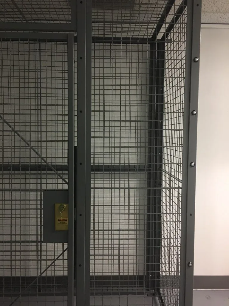 Close view of a welded wire mesh security cage door with a locking hasp and diagonal bracing