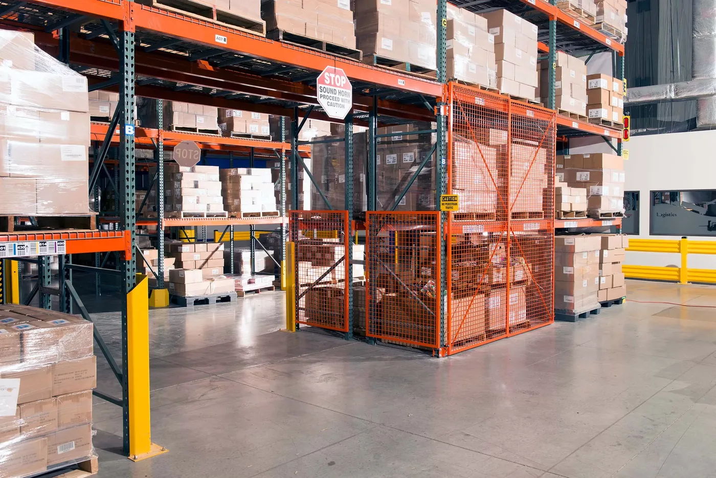 Wire mesh security enclosure built into a pallet rack bay on a plant floor