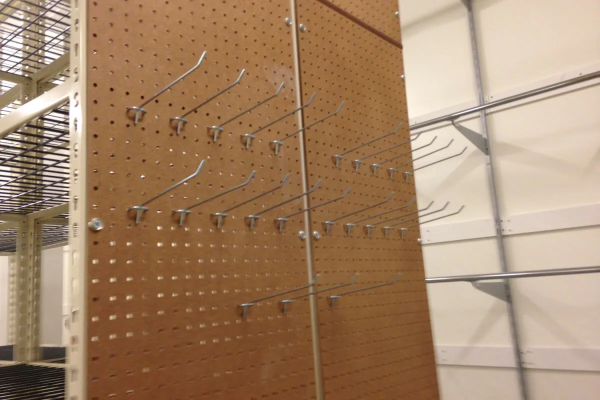 Pegboard end panel with hooks used to hang stockroom supplies beside a shelving run