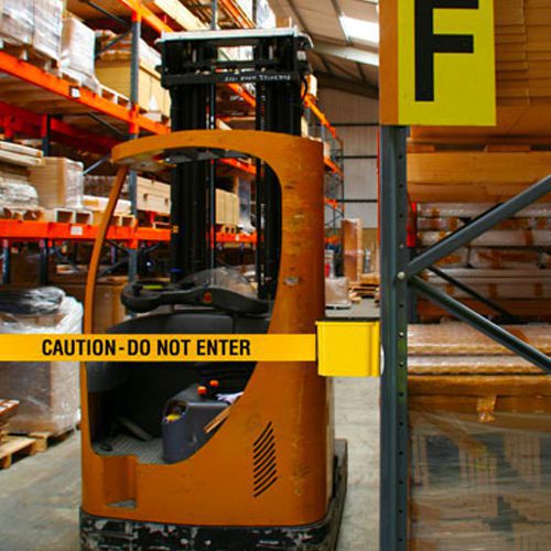 Yellow caution belt from a wall mounted retractable barrier blocking a forklift charging area in a warehouse