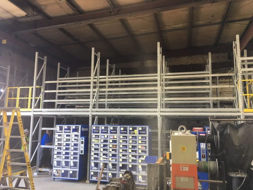 Steel mezzanine structure installed above shelving inside an existing warehouse building