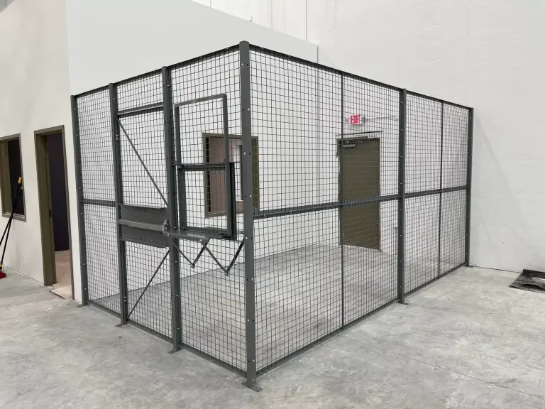 Gray wire mesh will-call security cage with a service window in a warehouse