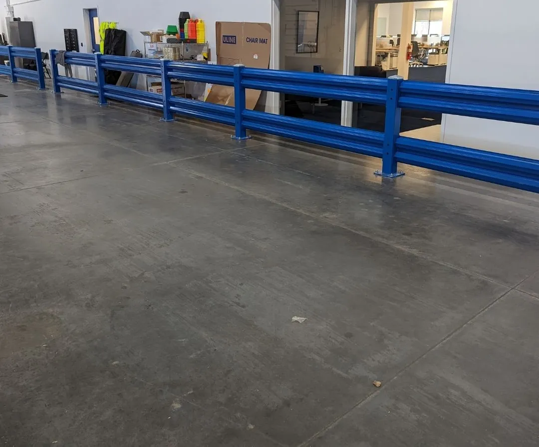 Blue double-rail steel guardrail separating an office and staging area from the warehouse forklift aisle