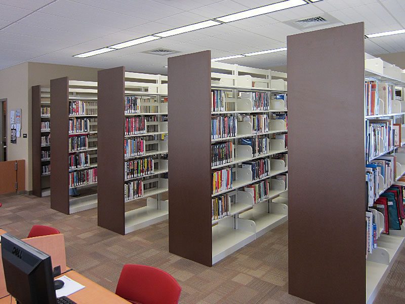 Double-sided cantilever library shelving stacks filled with hardcover books and brown end panels