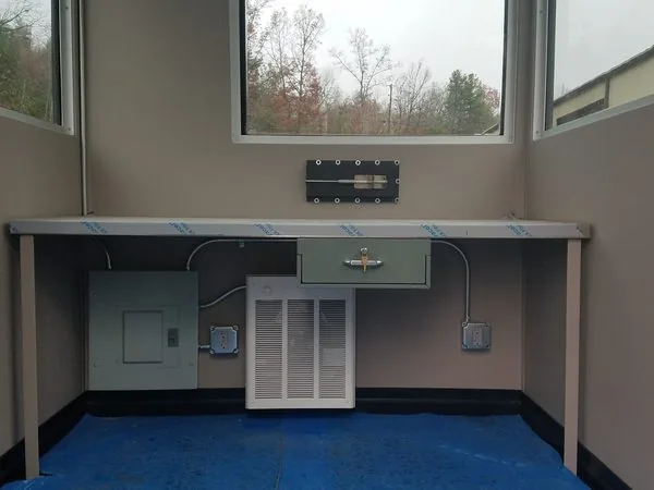 Guard booth interior showing the electrical panel, wall heater, outlets, transaction drawer and work counter