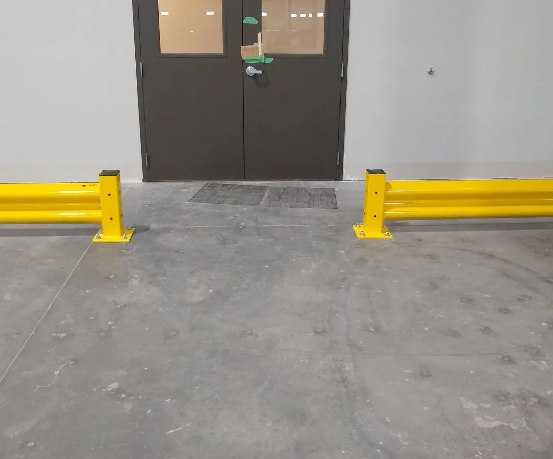 Heavy-duty yellow guardrail runs stopping short of a double door, leaving a clear landing in front of the entrance