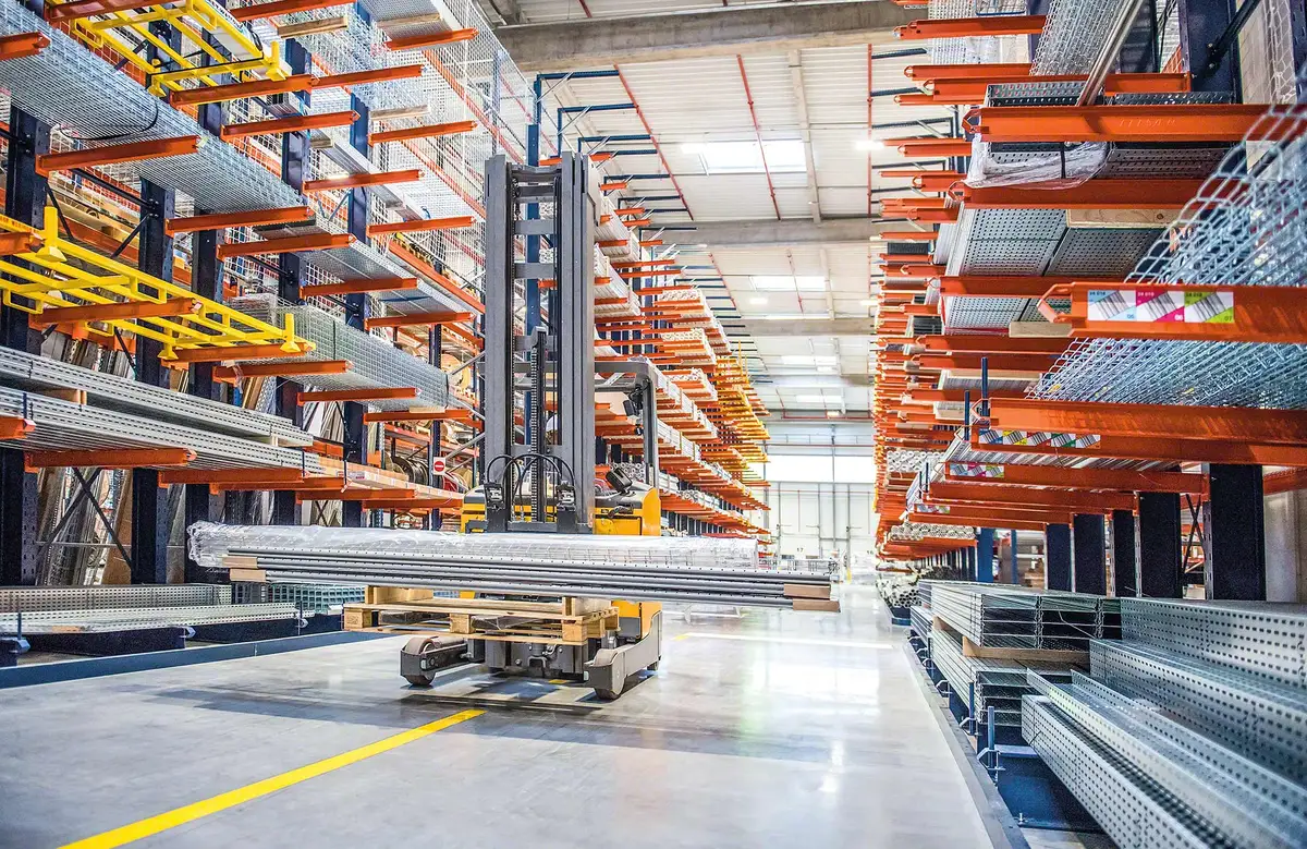 Structural cantilever racks holding heavy steel profiles and cable tray along both sides of a forklift aisle