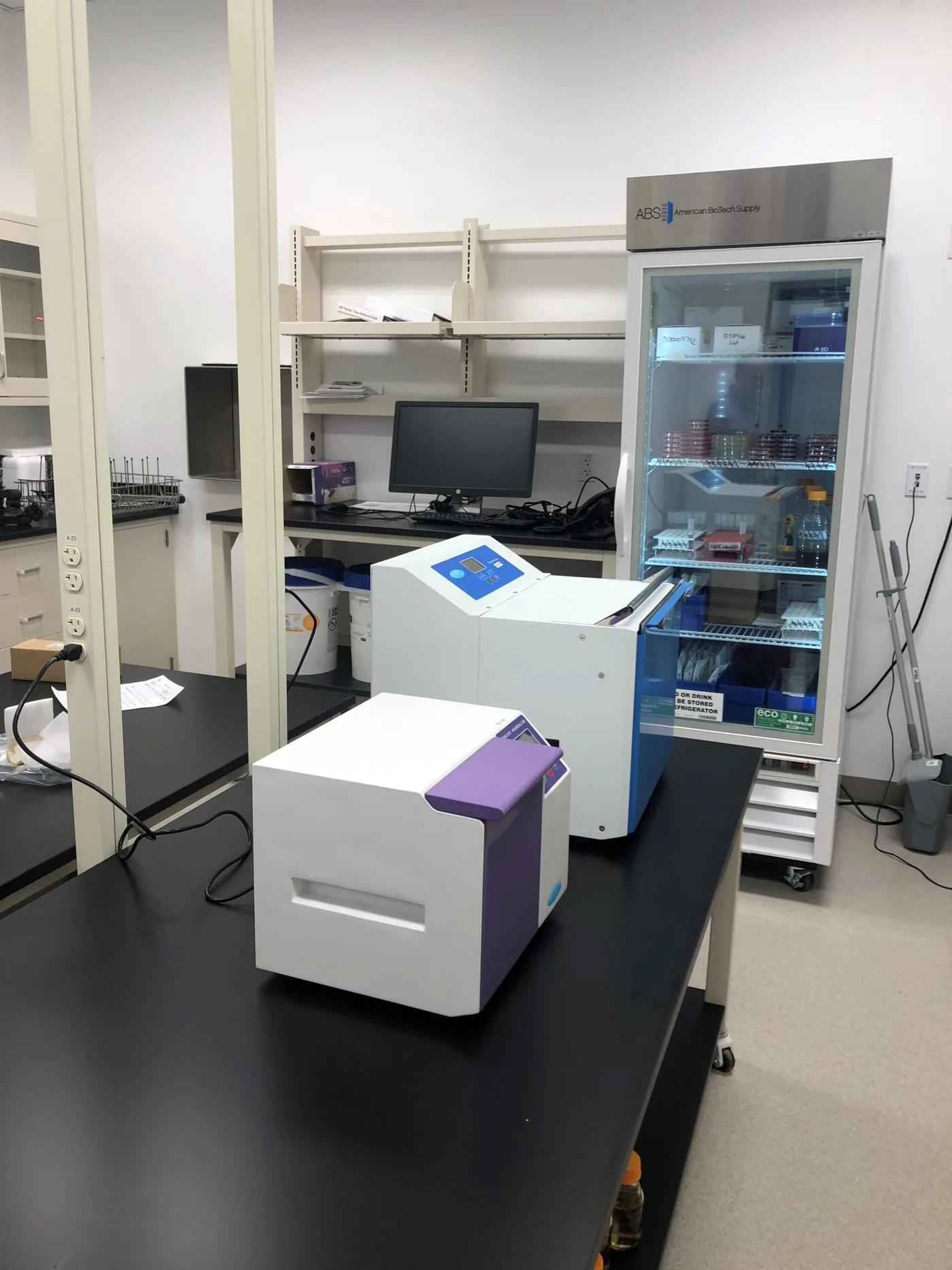 Working laboratory with black resin countertops, benchtop instruments and a glass-door refrigerator