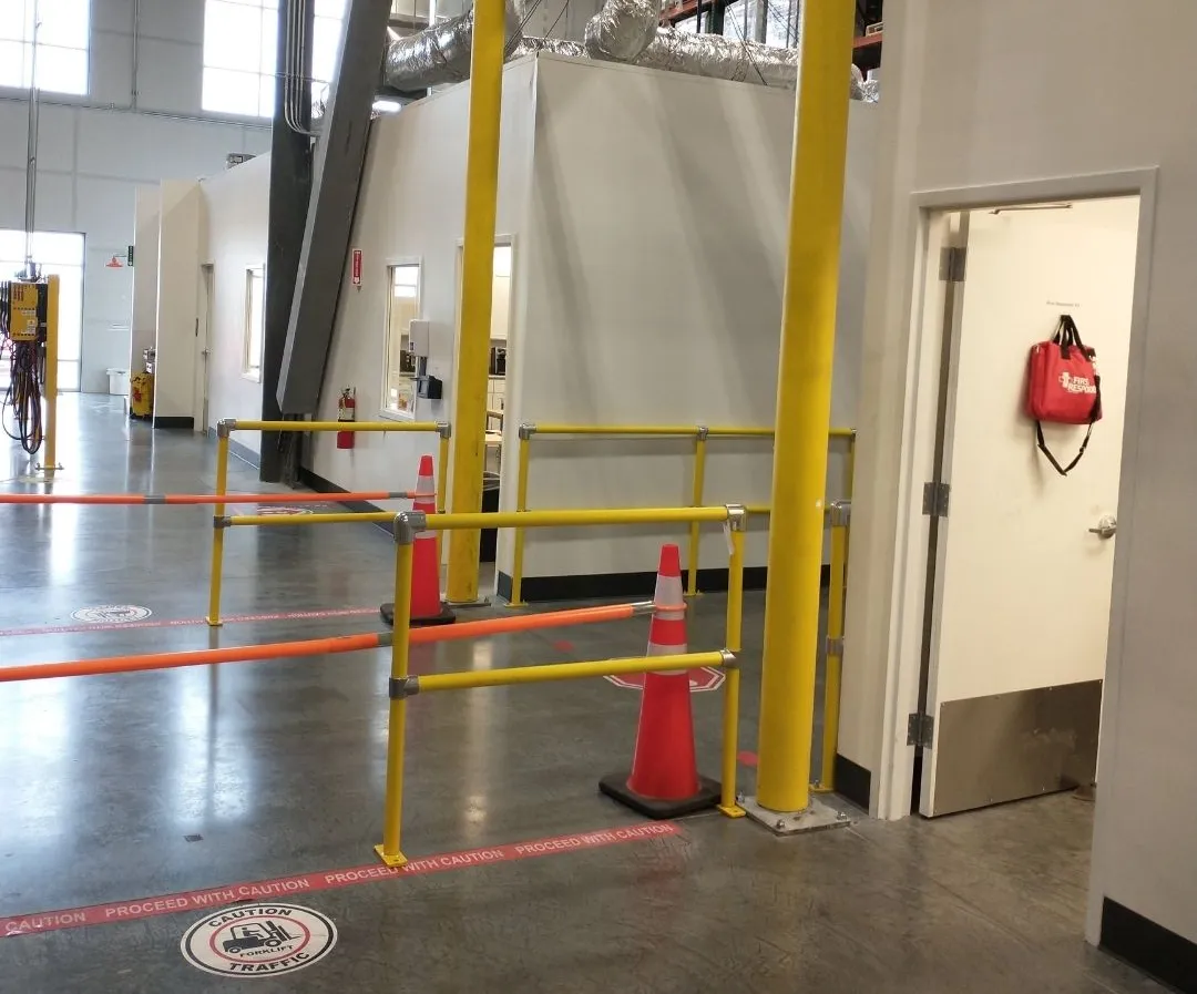 Plant room entrance protected by yellow steel guardrail, a railed pedestrian walkway and bollards