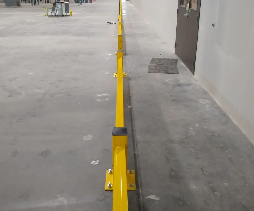 Long run of low-profile yellow guardrail anchored to the slab along an interior wall with a personnel door