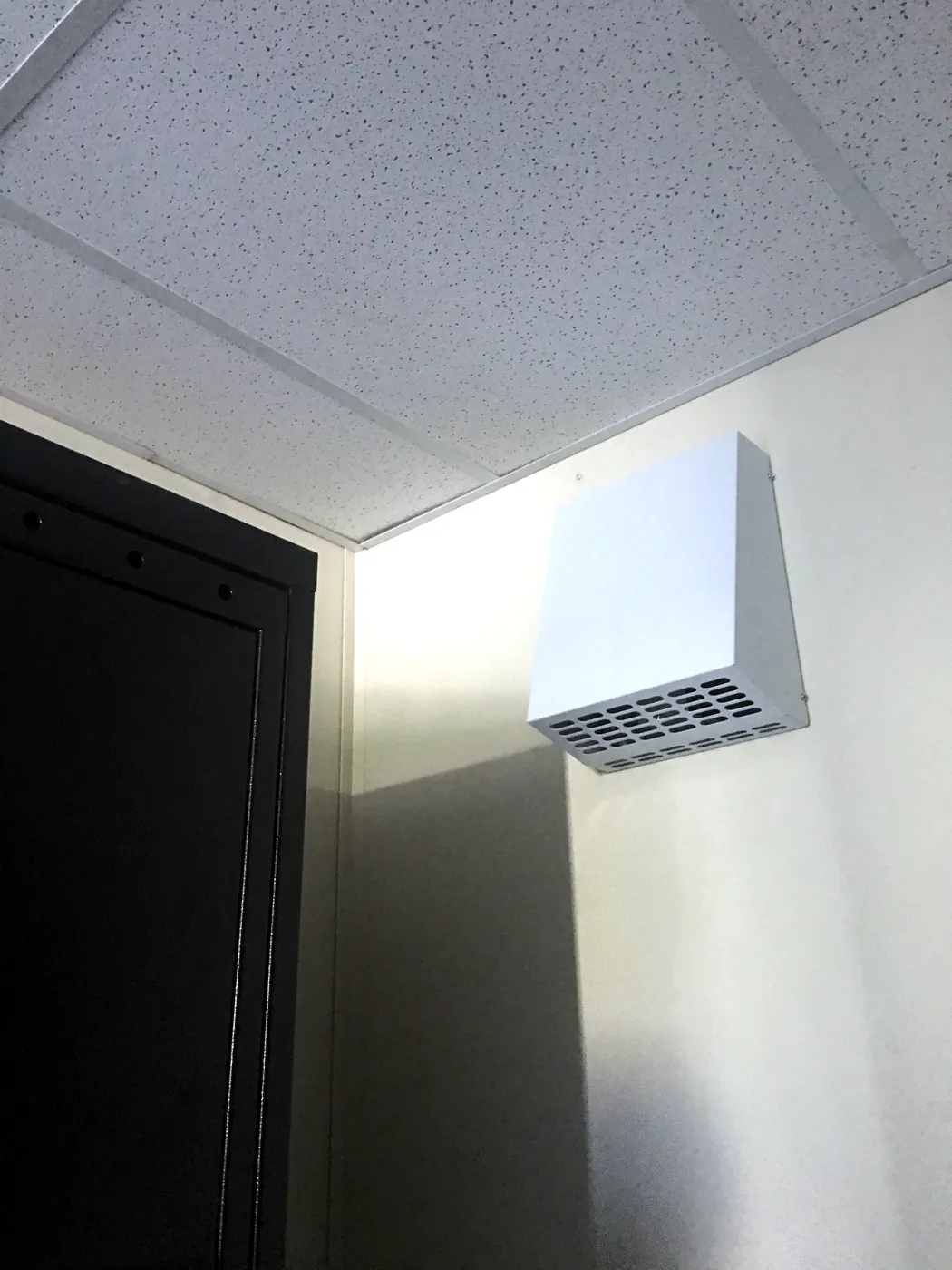 Wall-mounted exhaust fan below the lay-in ceiling of a modular change room